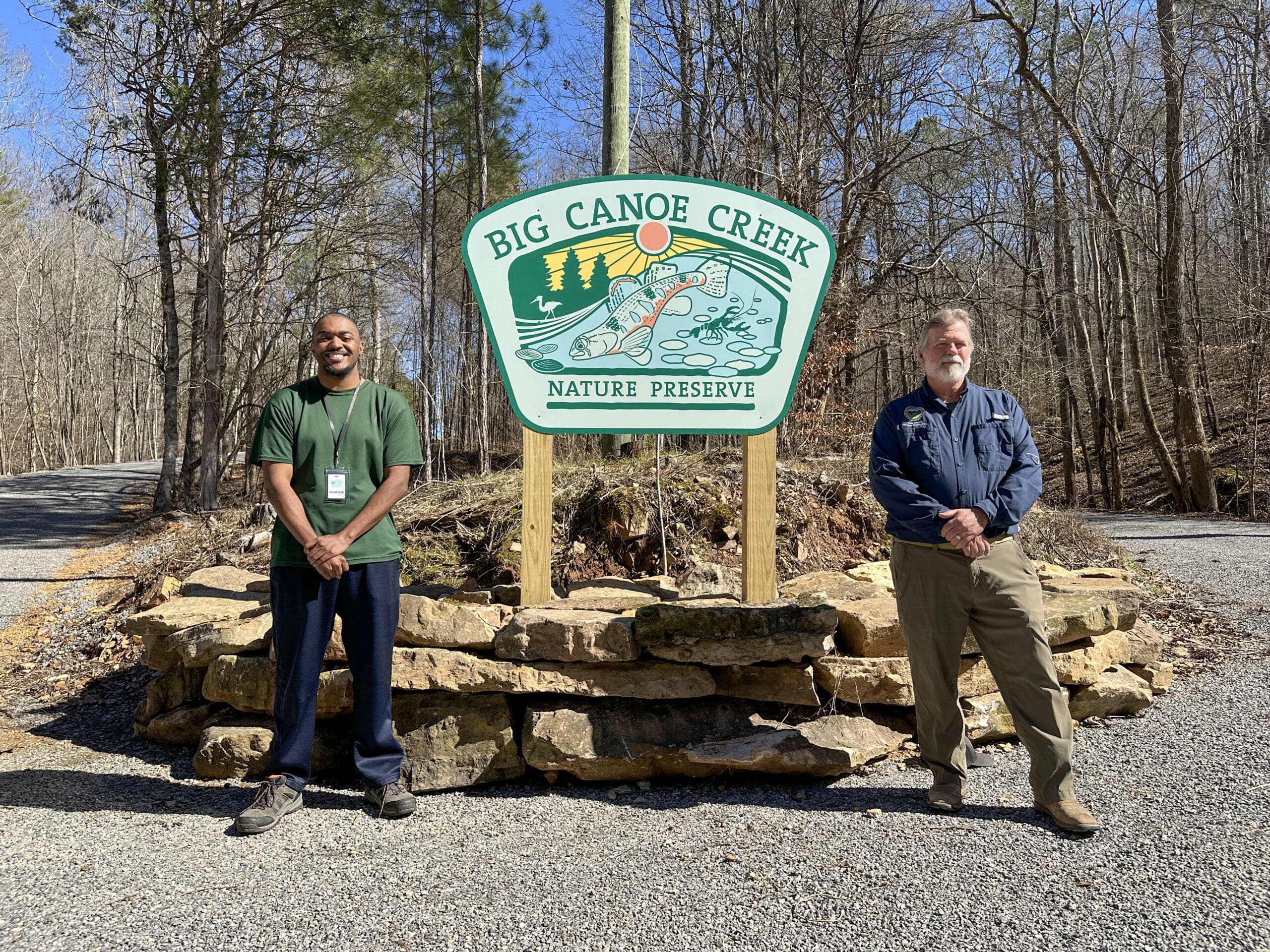 Two men standing in front of the entry sign at Big Canoe Creek in Springville, AL.