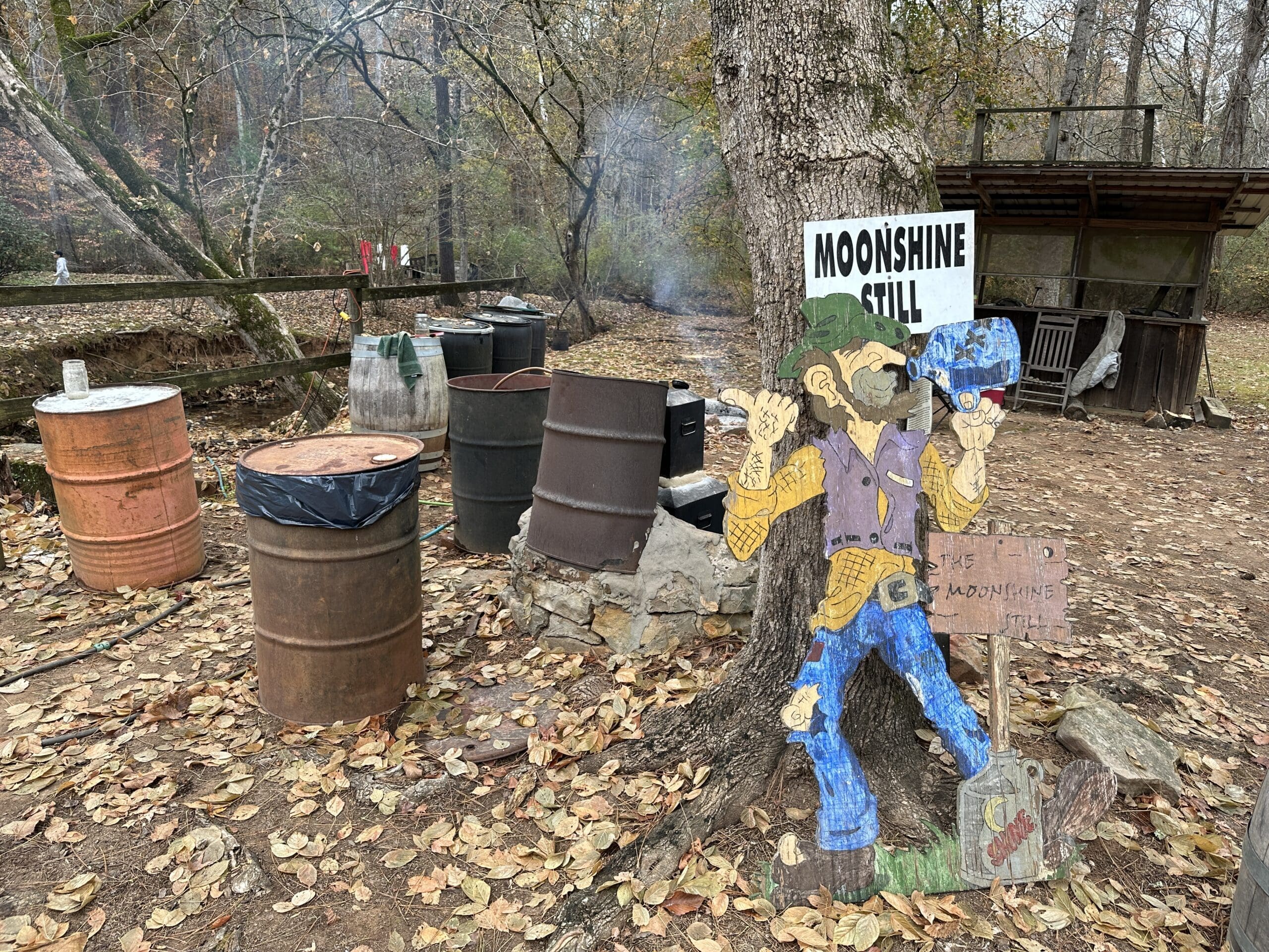 Moonshine still with a wooden cutout of a man drinking some from a bottle.