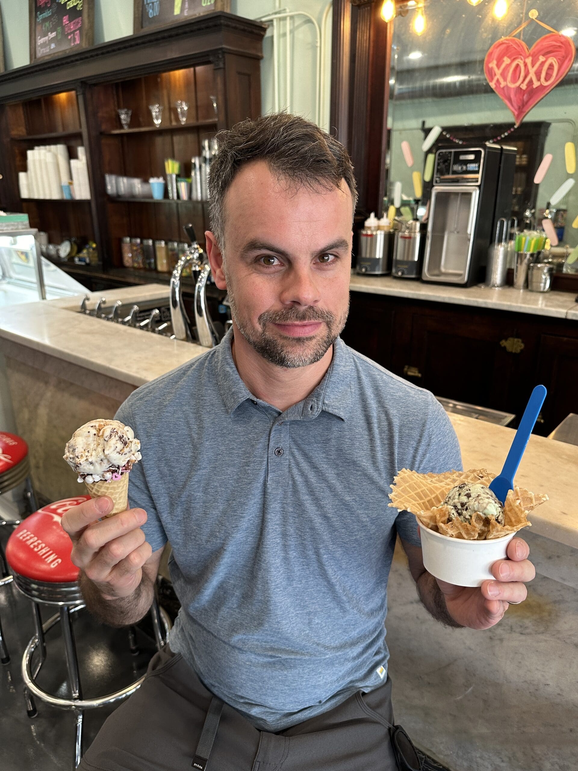 Man holding up an ice cream cone and an ice cream cup.