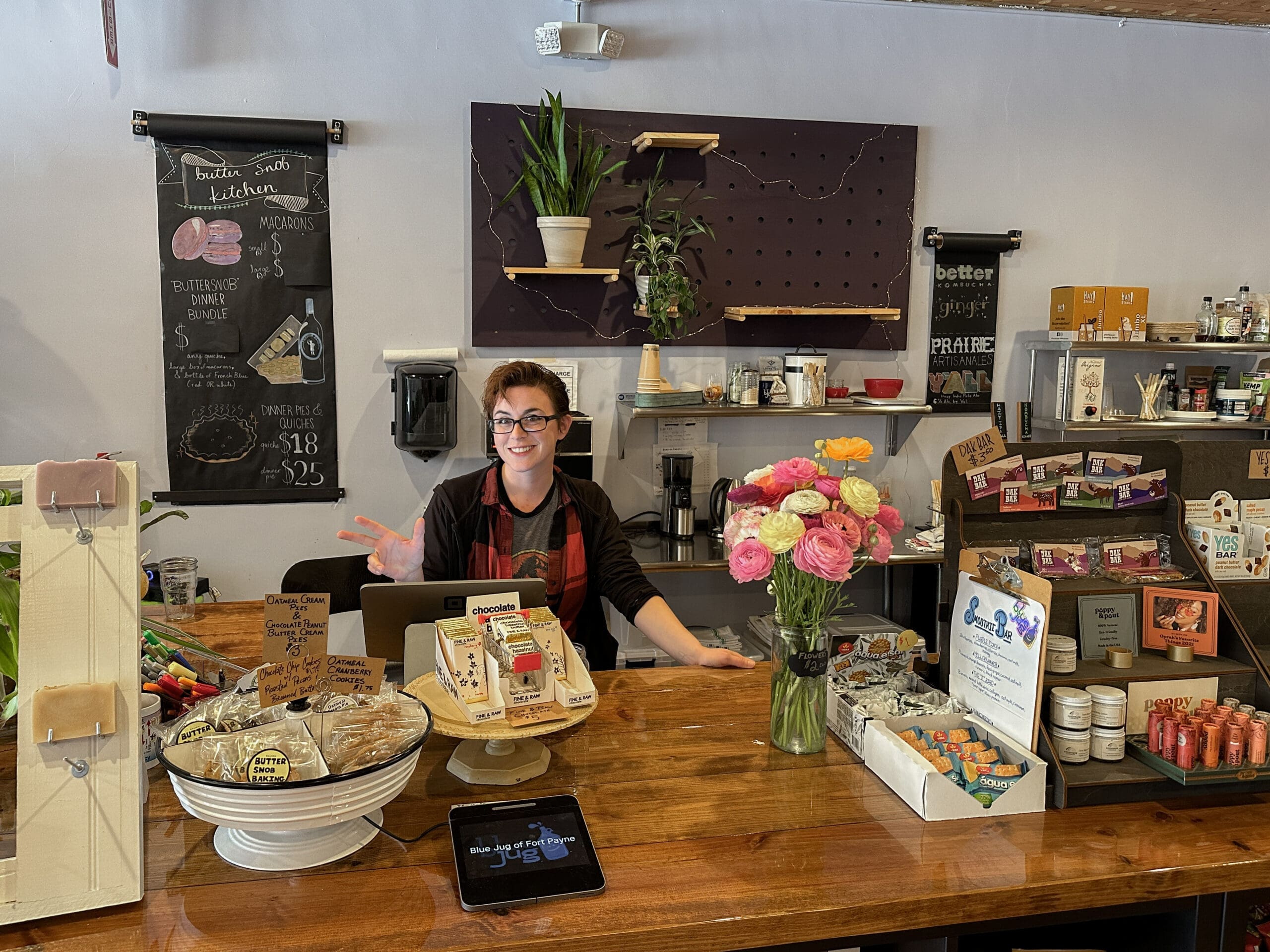 A woman behind a counter makes a peace sign at the camera.