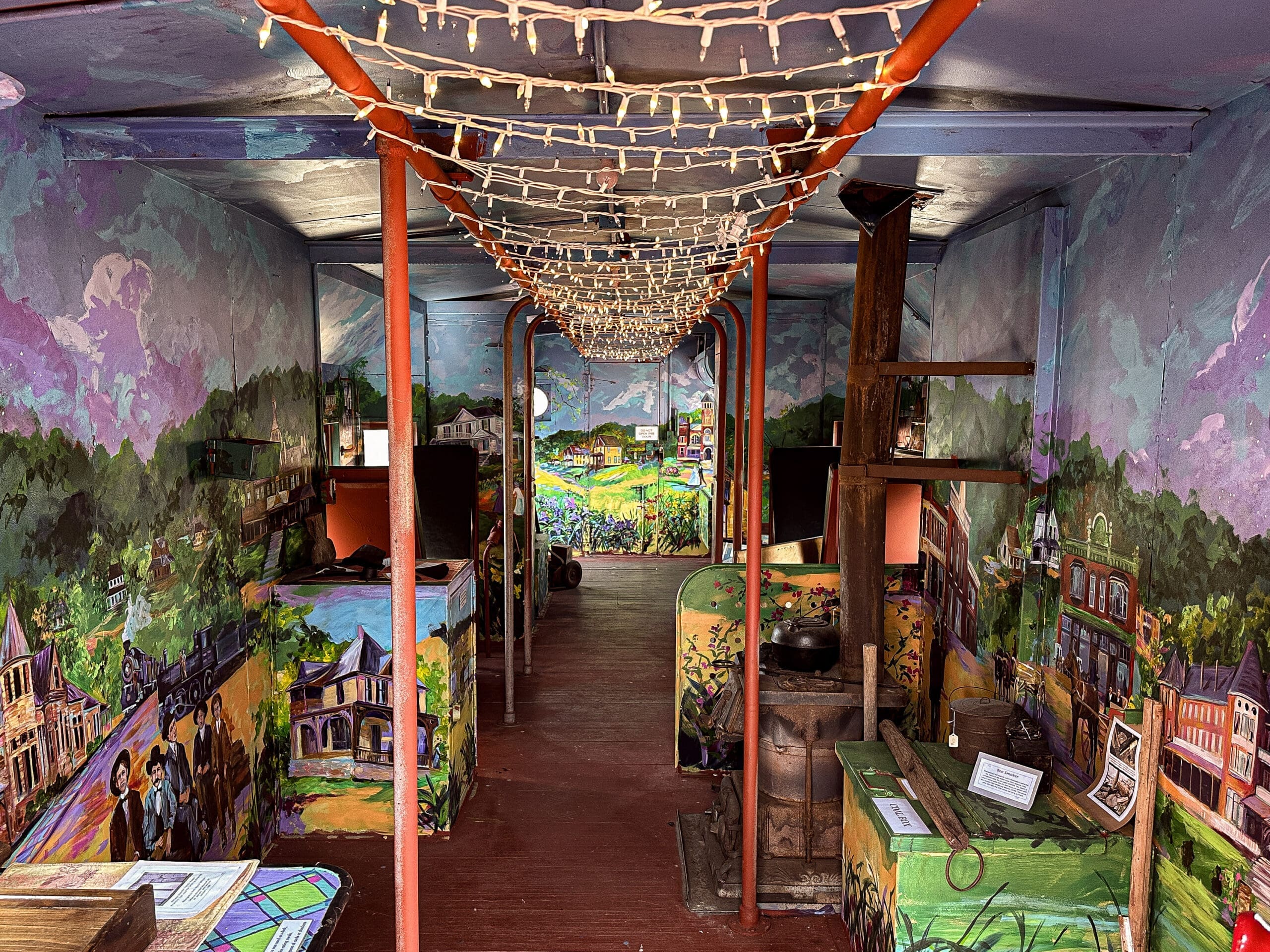 Interior of a caboose whose walls have been entirely painted with a mural featuring life in Fort Payne, AL in the late 1800s.