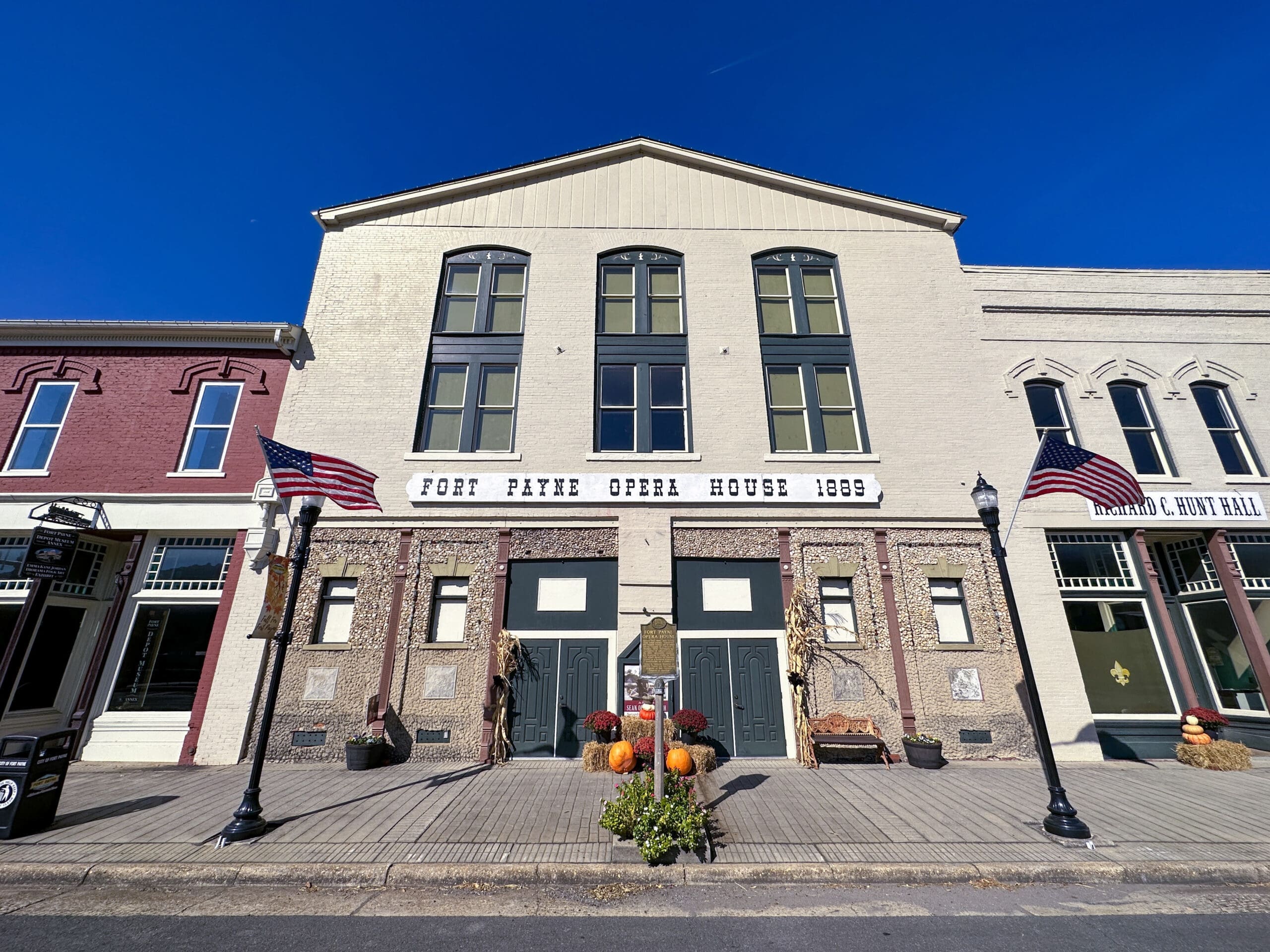 Street view of historic opera house with sign reading "Fort Payne Opera House 1889". American flags wave in front.