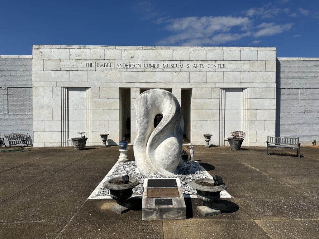 Front a museum with marble facade. Inscribed above doorway: Isabel Anderson Comer Museum. A large, wavy marble sculpture dominates the courtyard in front.