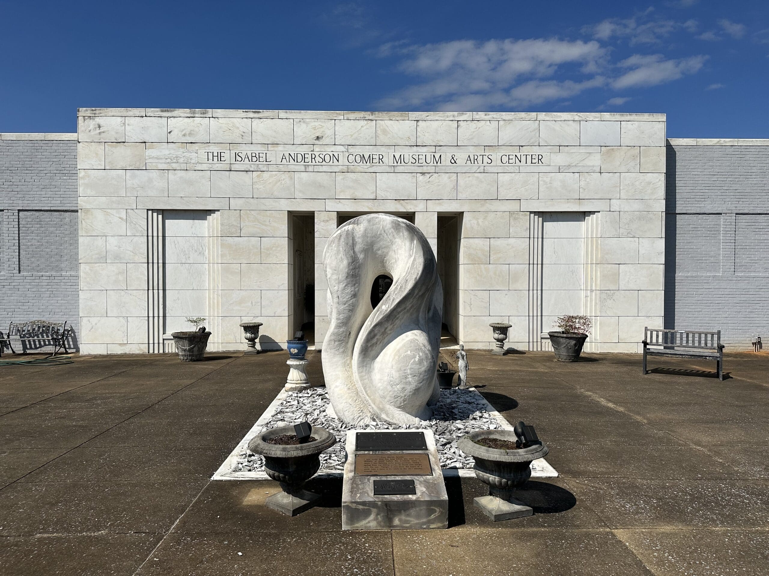 Front a museum with marble facade. Inscribed above doorway: Isabel Anderson Comer Museum. A large, wavy marble sculpture dominates the courtyard in front.