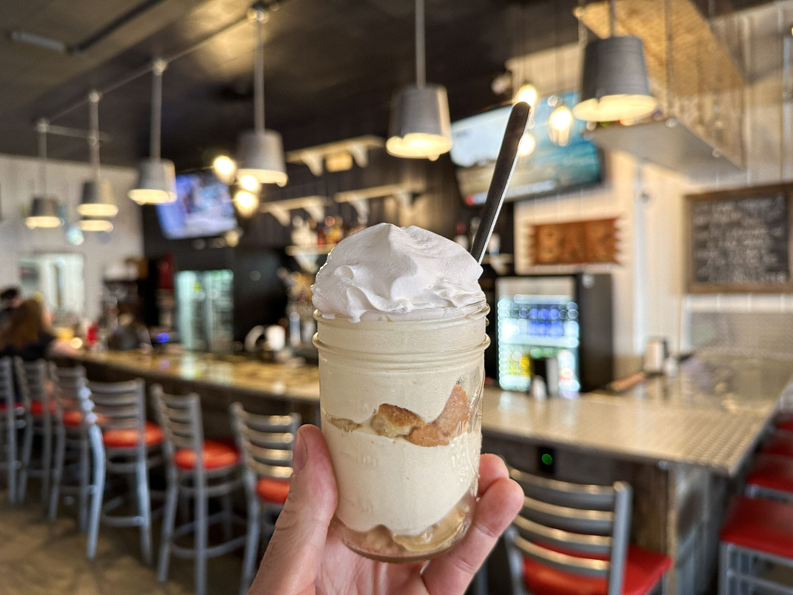 A hand holding up a small mason jar filled with banana pudding.