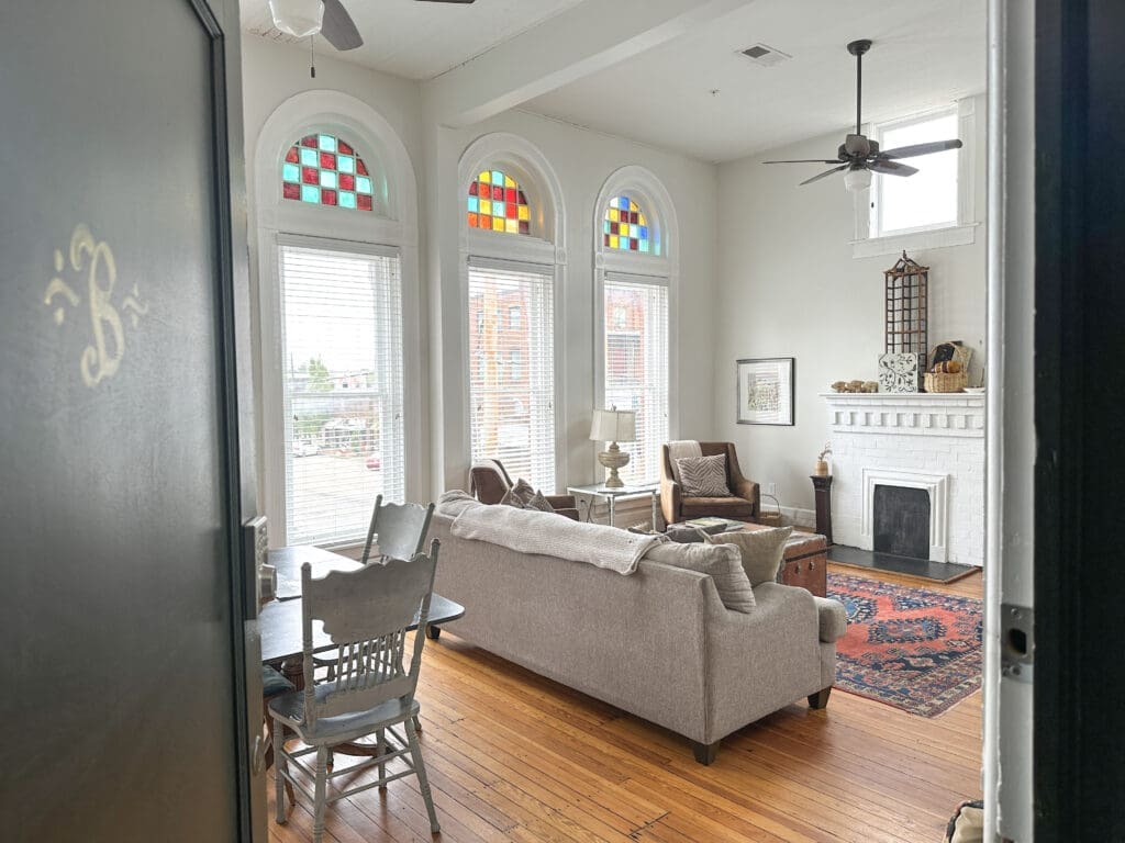 Photo taken while entering a door into a second-story AirBNB rental with white wall paint, fireplace, and large windows with colorful transoms.