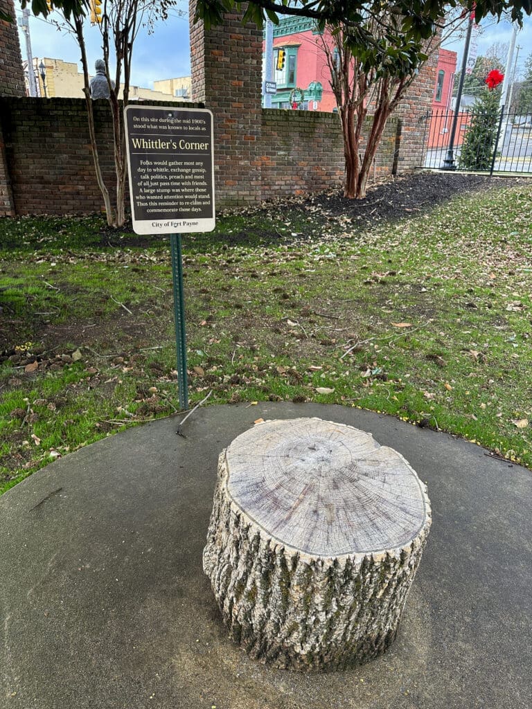 A preserved stump in a public park with a sign behind it reading "Whittler's Corner".