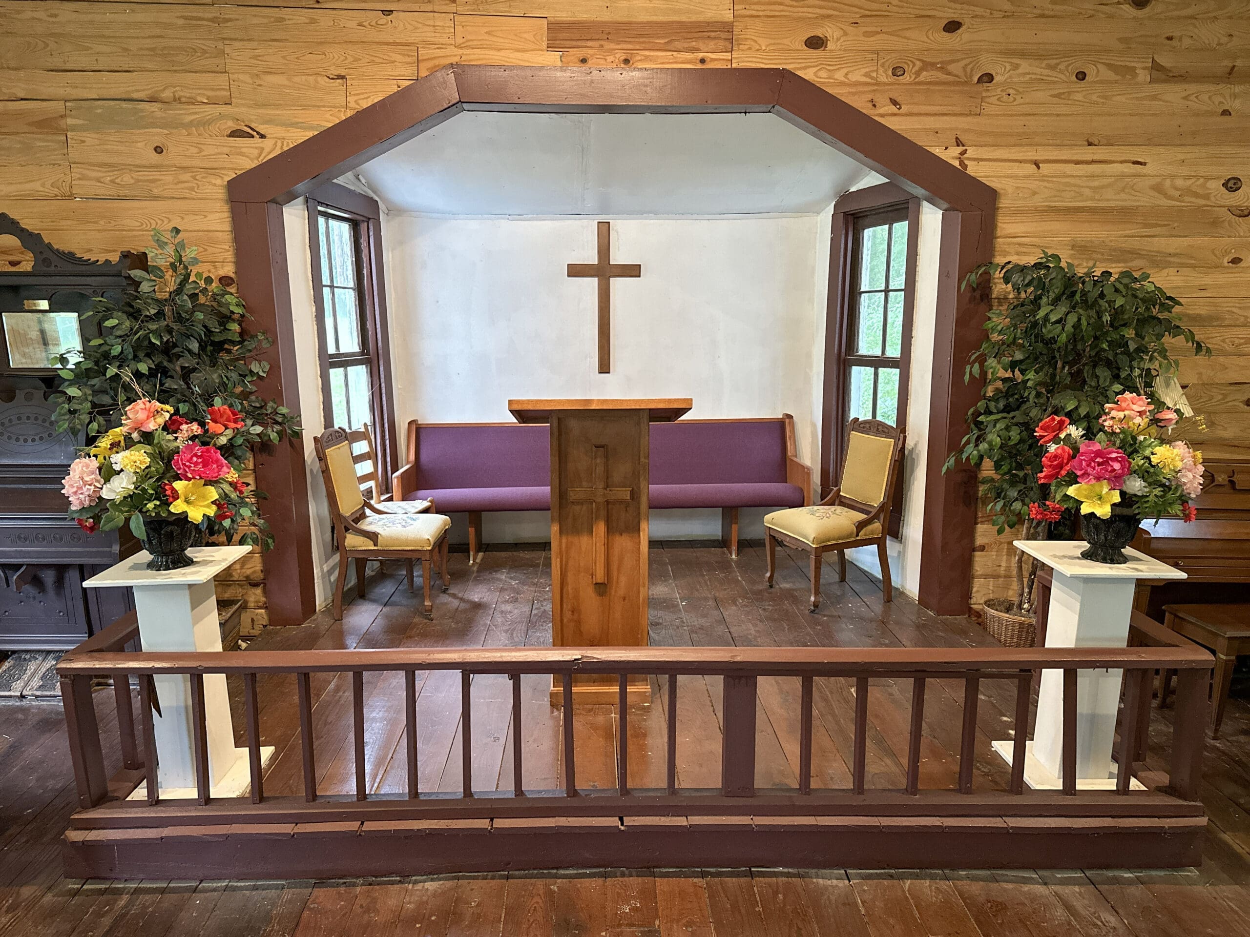 Small sanctuary and altar in historic rural church. Flower arrangements on each side and a cross hanging at the back.