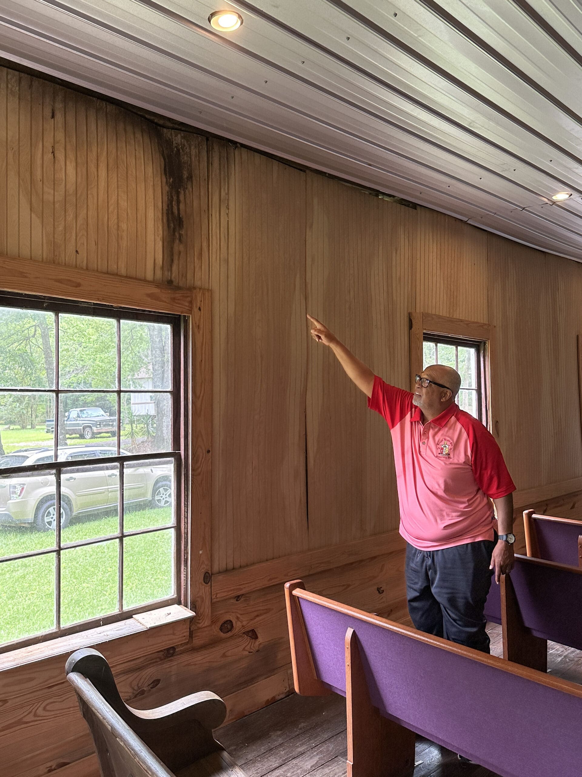 A man points to water damage along the ceiling in a rural, historic Black church.