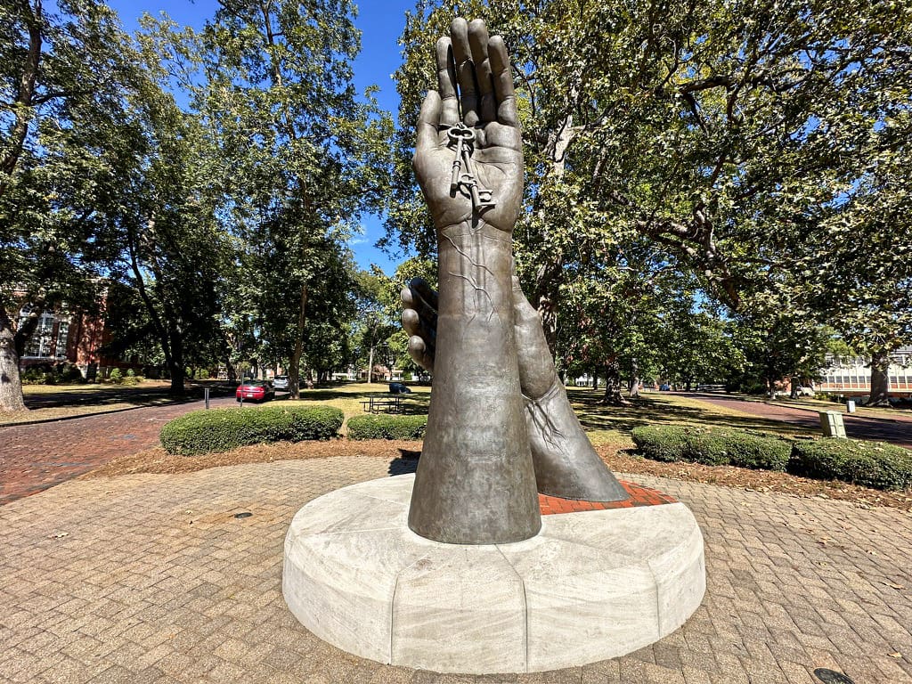 A 16-foot tall bronze sculpture of two hands, one upright holding a key and another reaching upward toward it.