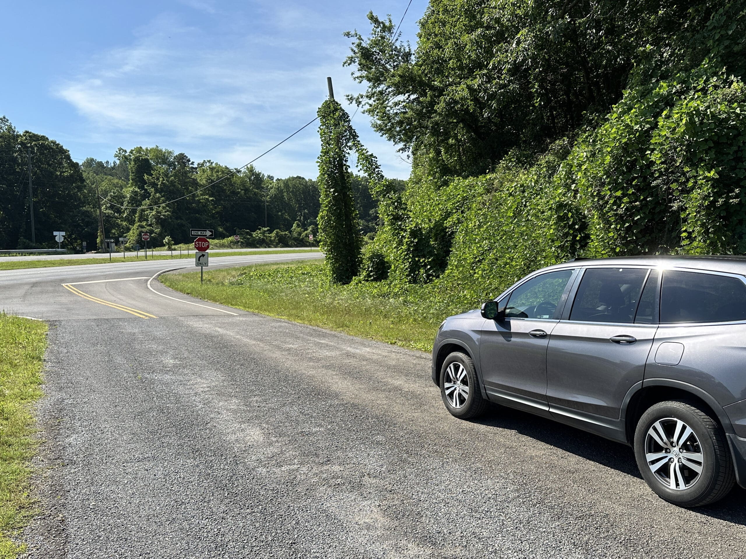 A grey car faces downhill towards a STOP sign at a crossing four-lane highway.