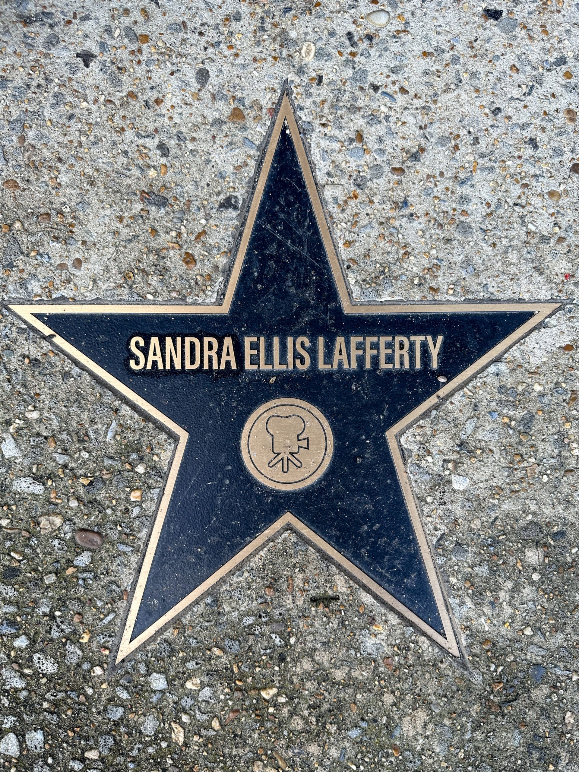 A "walk of fame" sidewalk star that reads "Sandra Ellis Lafferty". Beneath the name is a symbol of a classic movie theatre projector.