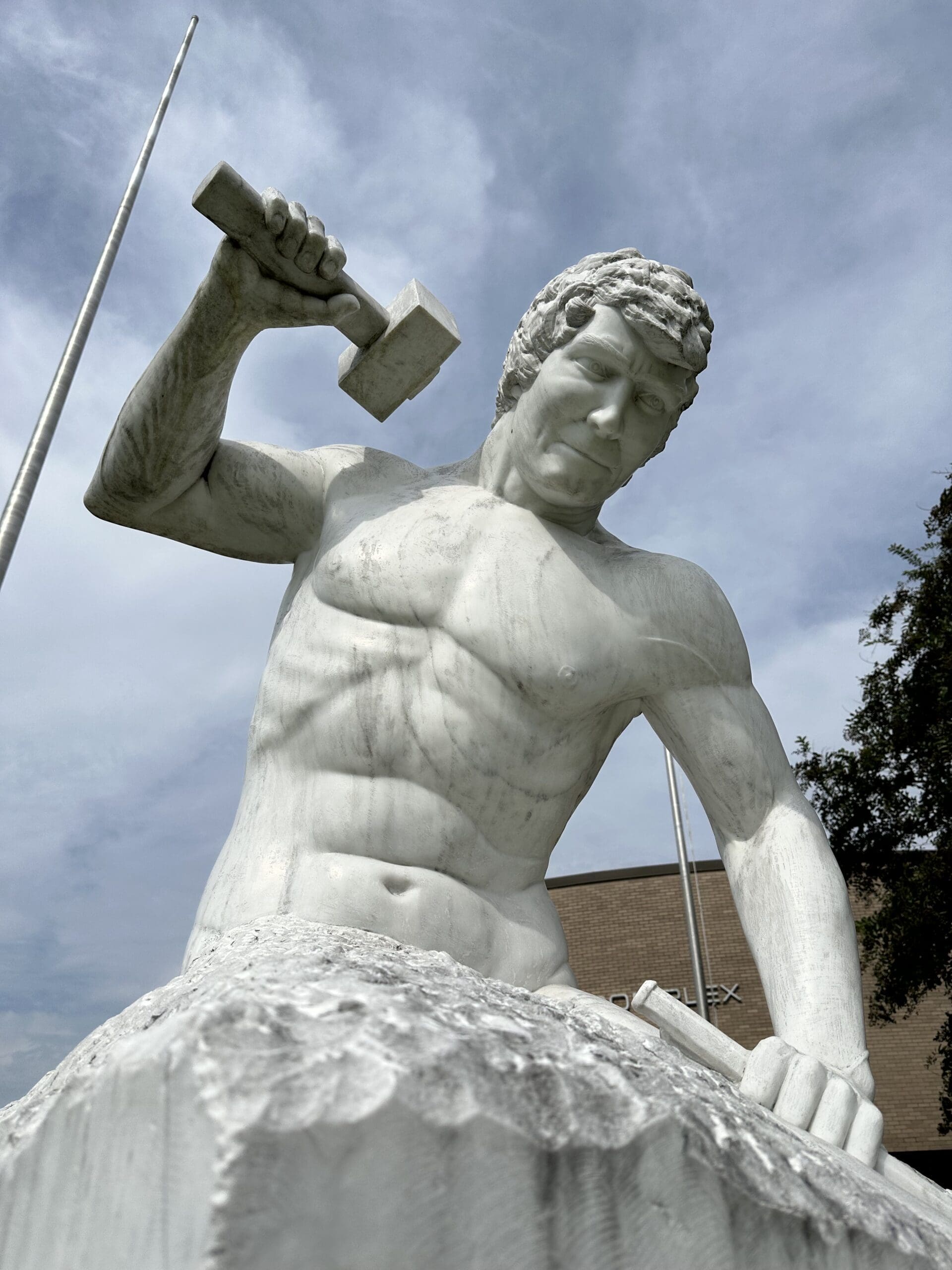 A large marble sculpture of a man carving himself out of marble. While his body from the waist up has already been carved, his bottom half is still a block of marble.