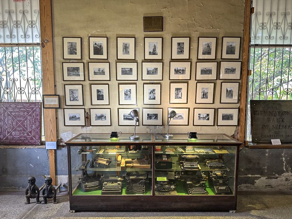 A collection of framed, black-and-white photos on a wall. Photos depict early 20th century, rural Black life around Selma, AL.
